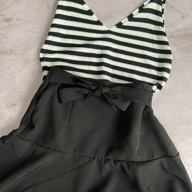 Top de rayas blancas y negras sujeto a una falda negra con lazo, sobre una superficie gris claro.