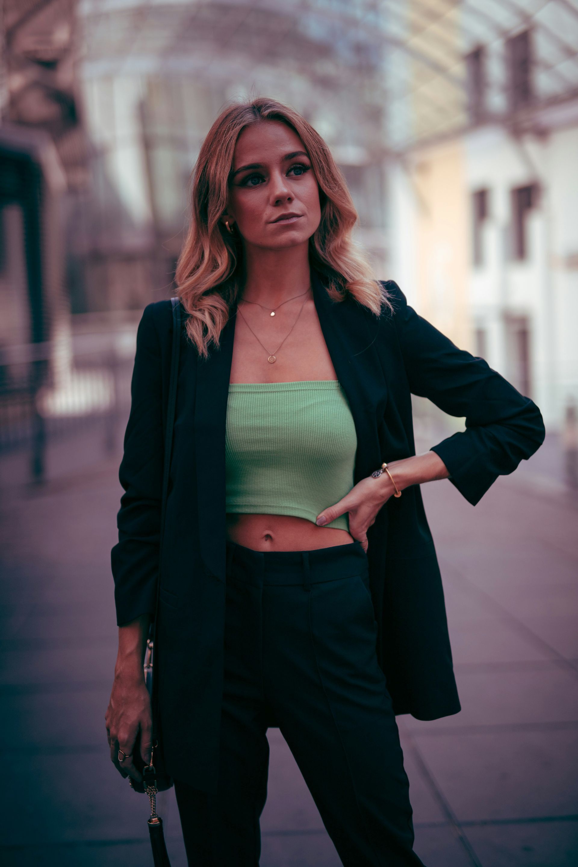 Una mujer con traje negro y top corto verde lima posa al aire libre, mirando hacia otro lado.