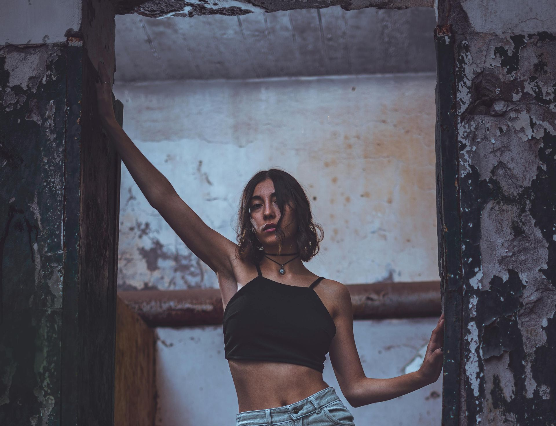 Una mujer con un top negro posa en una puerta en ruinas, con el brazo extendido.