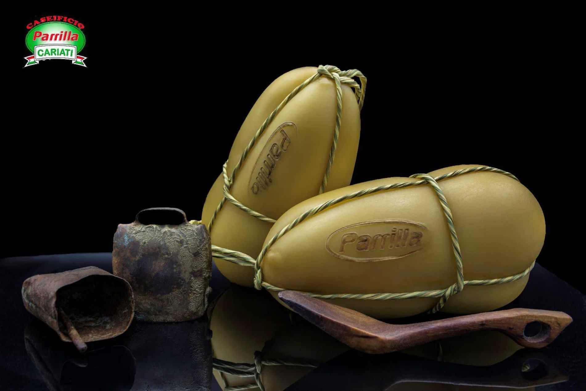 Due pezzi di formaggio appoggiati su un cucchiaio di legno accanto a una campana