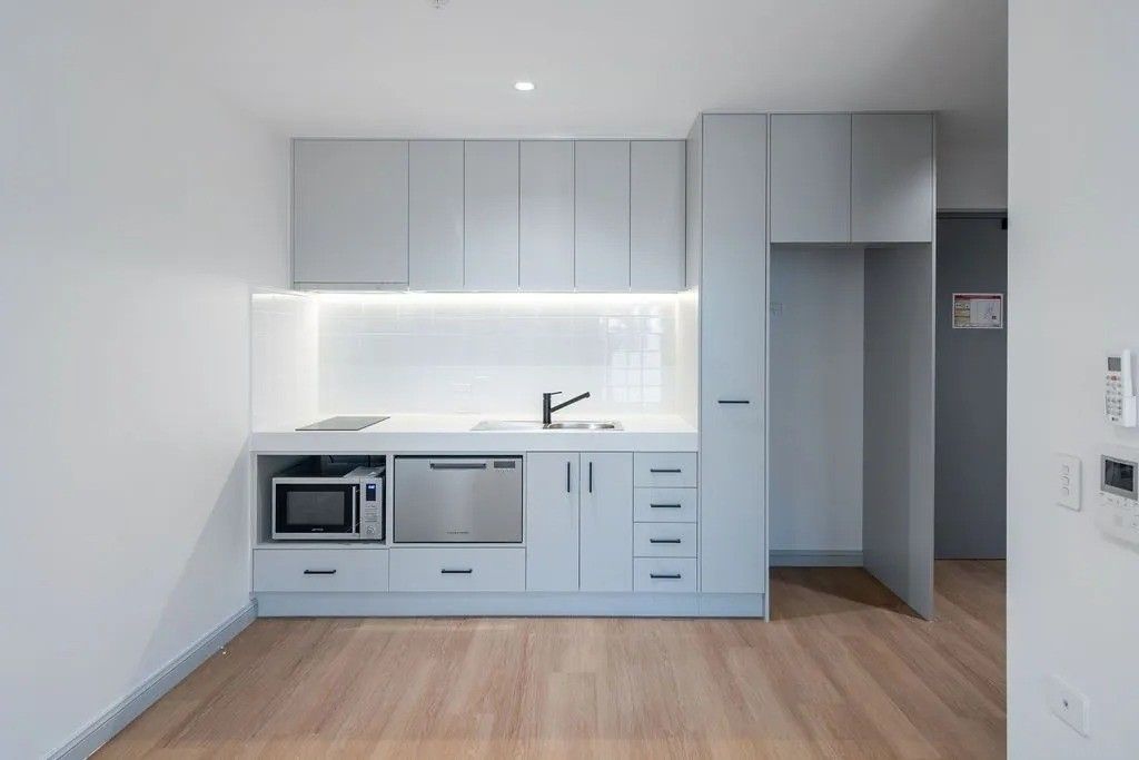 Small, modern, light grey kitchen in a studio apartment with microwave, sink, and cabinets; wood floor.