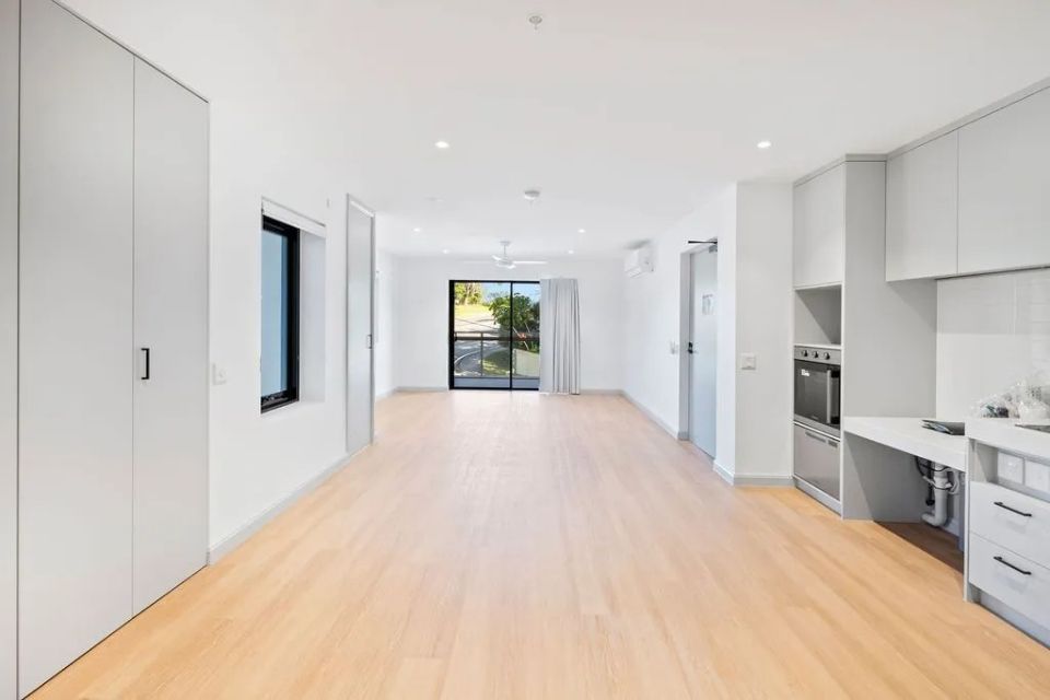 Bright, modern apartment interior with light wood flooring, gray cabinetry, and a sliding glass door to a balcony.