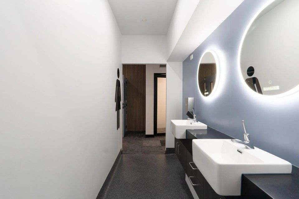 Modern public restroom with two sinks, circular mirrors with backlighting, and a dark floor.