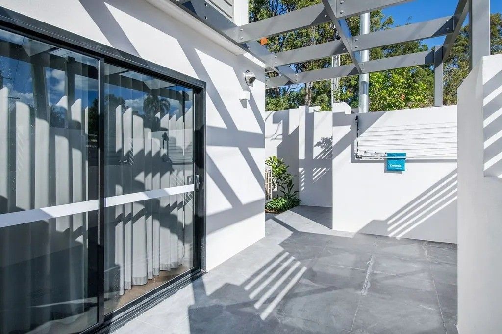Exterior view of a modern white building with a sliding glass door and a shaded patio area.