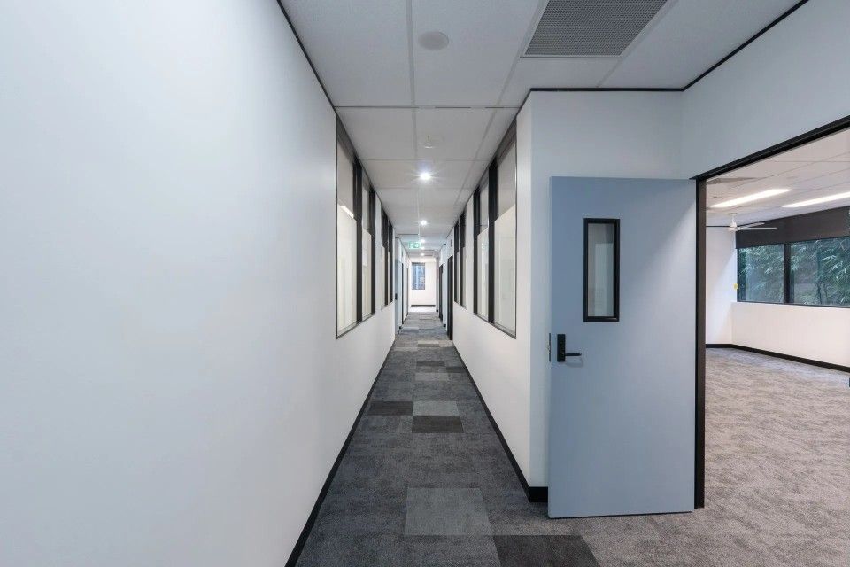Narrow office hallway with white walls, gray carpet, and a blue door.