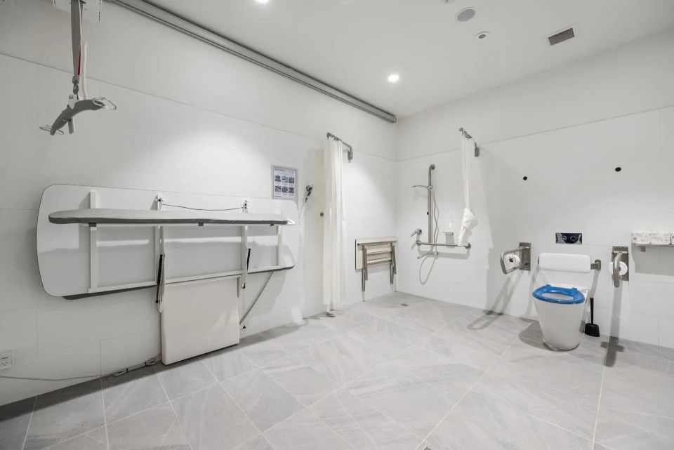 Accessible restroom with changing table, toilet, and shower. White walls and tiled floor.