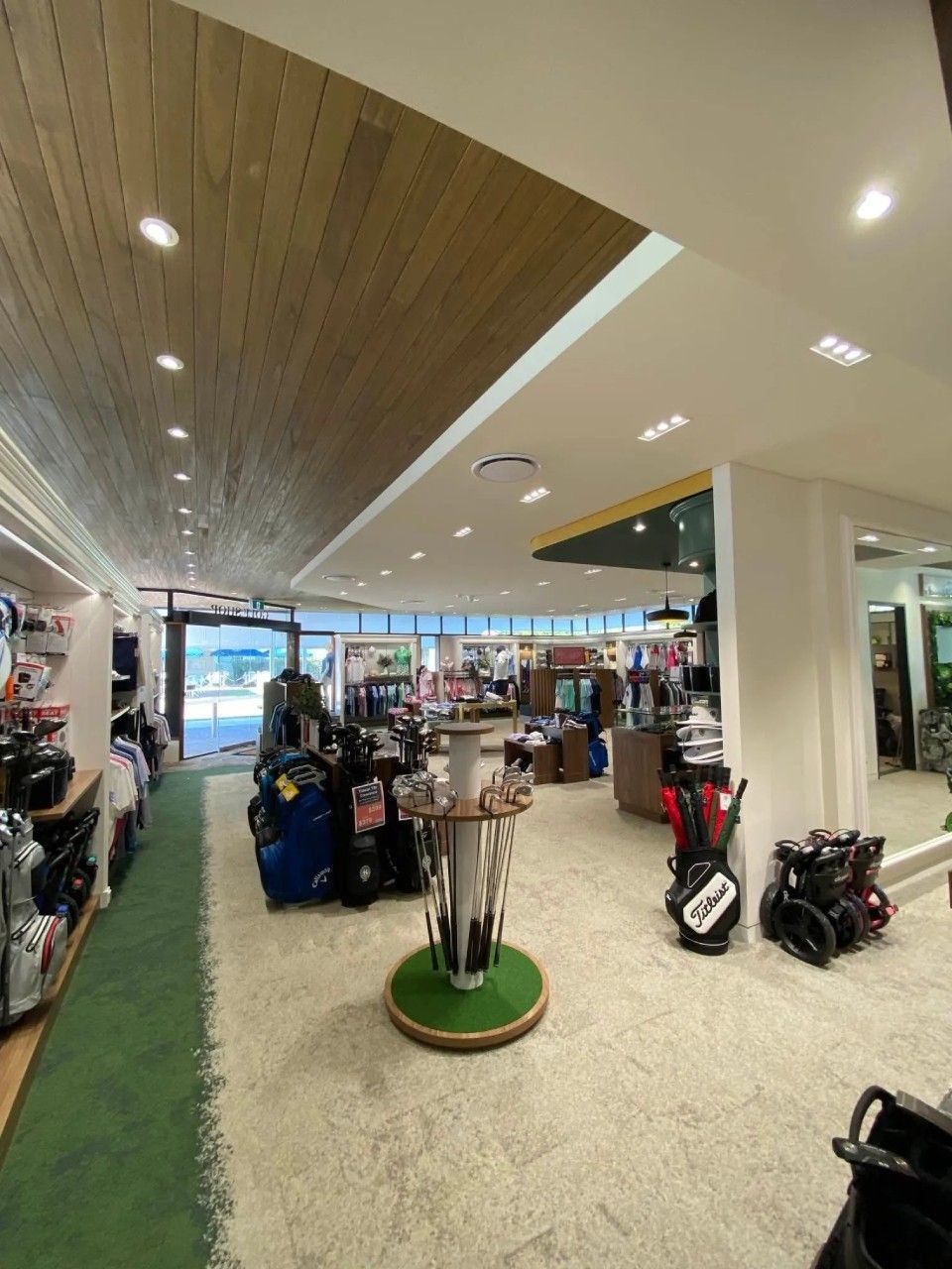 Golf equipment store interior, various items on display, including golf bags and clubs. Brightly lit with green and white accents.