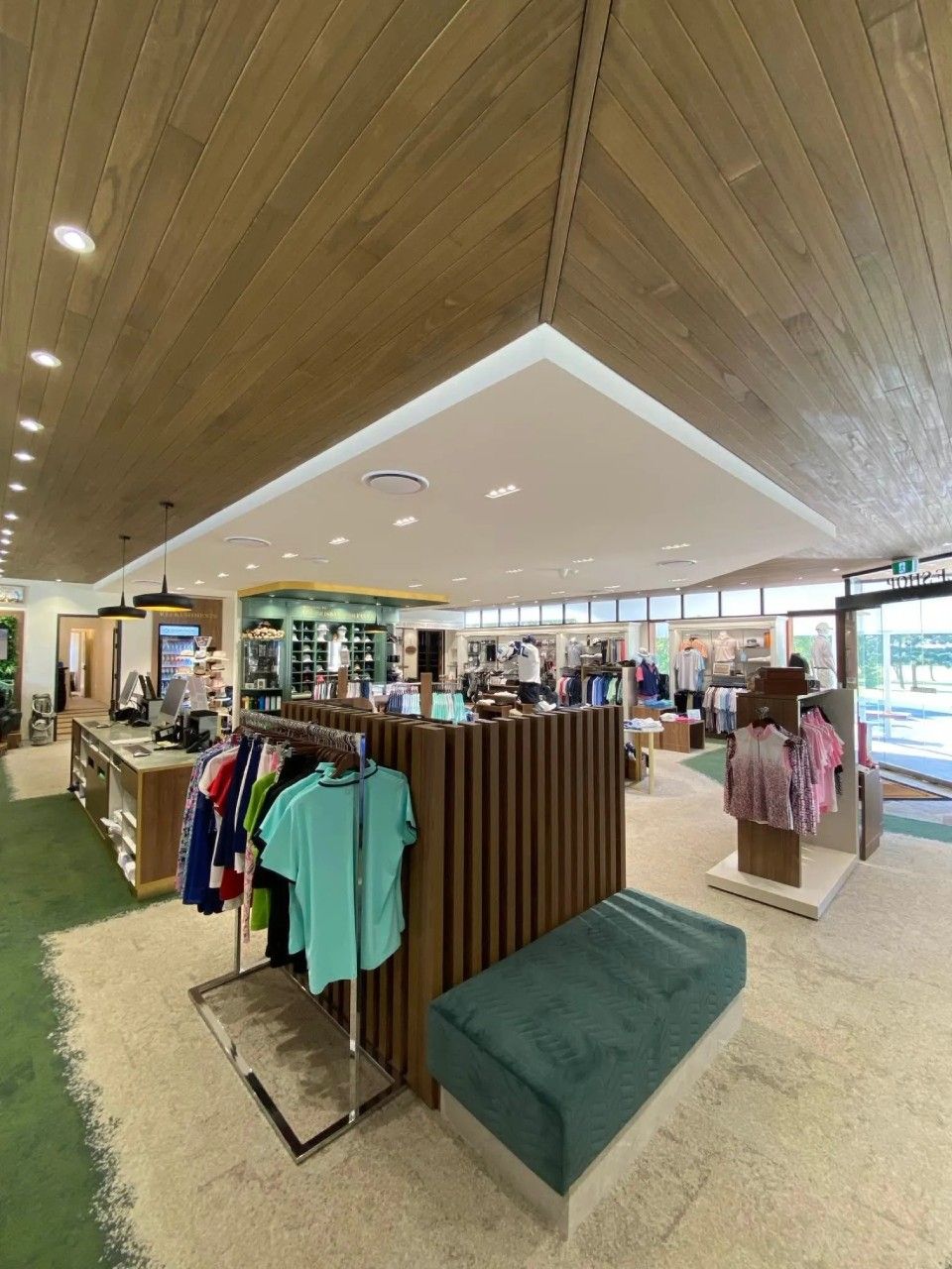 Interior shot of a golf shop with clothing racks, a green bench, and wooden accents.