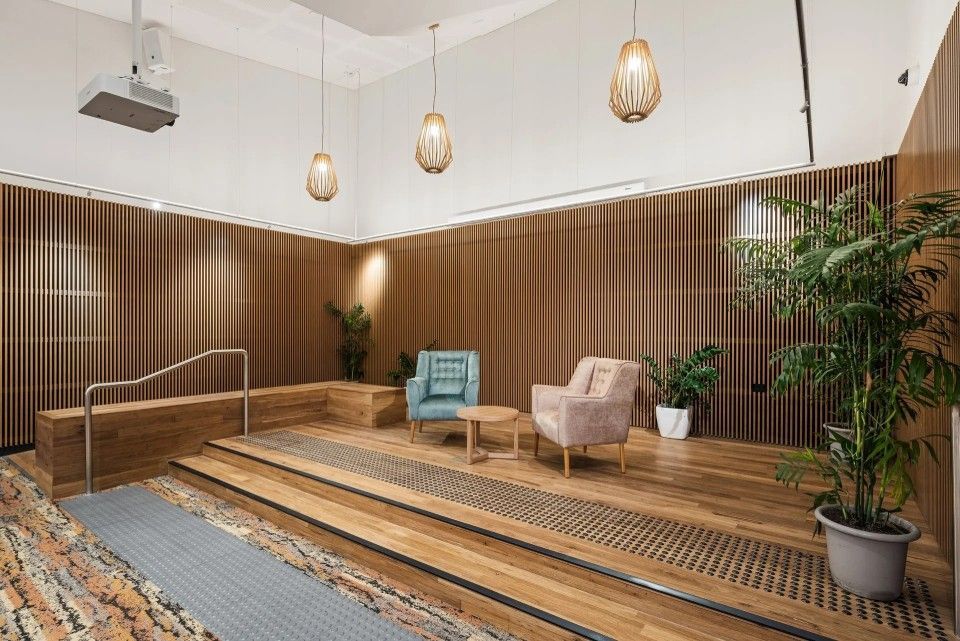 A raised wooden platform with seating, plants, and hanging lights in a room with brown wall panels.