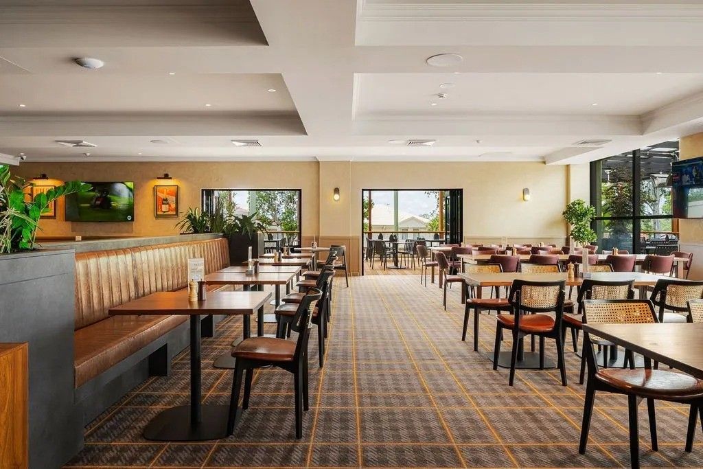 Restaurant interior with tables, chairs, and booths; open doors to a patio.