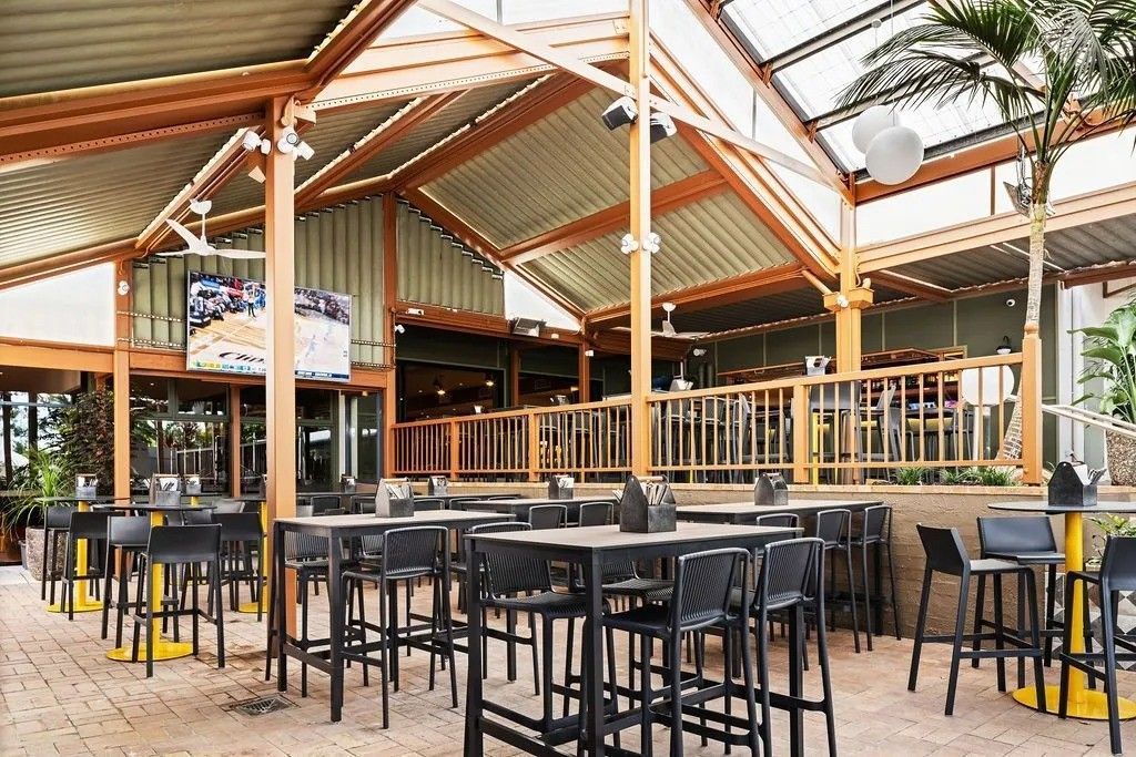 Outdoor restaurant with black tables, stools, and a wooden roof structure.