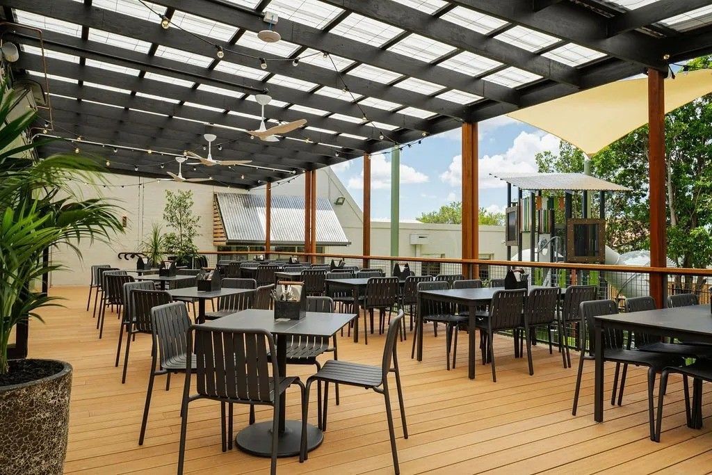 Outdoor restaurant patio with tables and chairs under a shaded canopy.