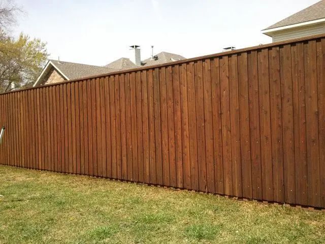 Brown wooden fence in a grassy yard, with rooftops visible in the background.