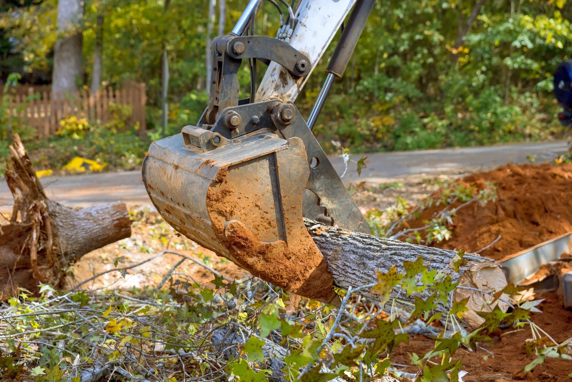Excavator bucket lifting a tree stump from a construction site.