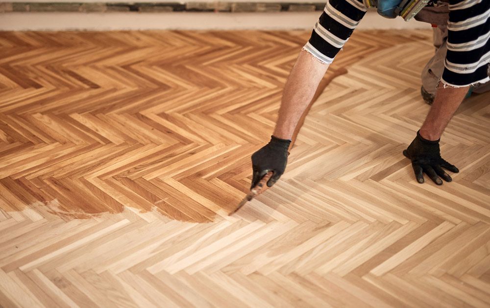 A Person is Painting a Wooden Floor With a Brush — Coastline Floor Sanding in Wyong, NSW