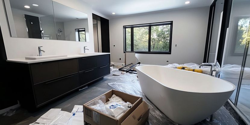 Modern bathroom under construction, features a large soaking tub, dark vanity, and large window.