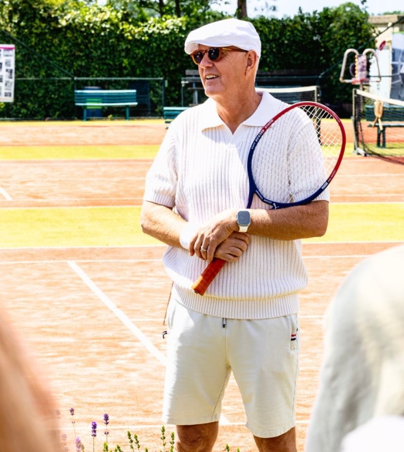Twee mannen staan ​​op een tennisbaan met tennisrackets en een mand met tennisballen.