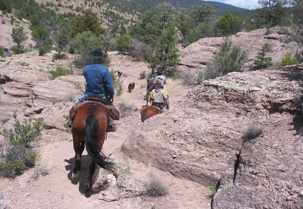 People on horseback riding through a rocky, desert landscape.