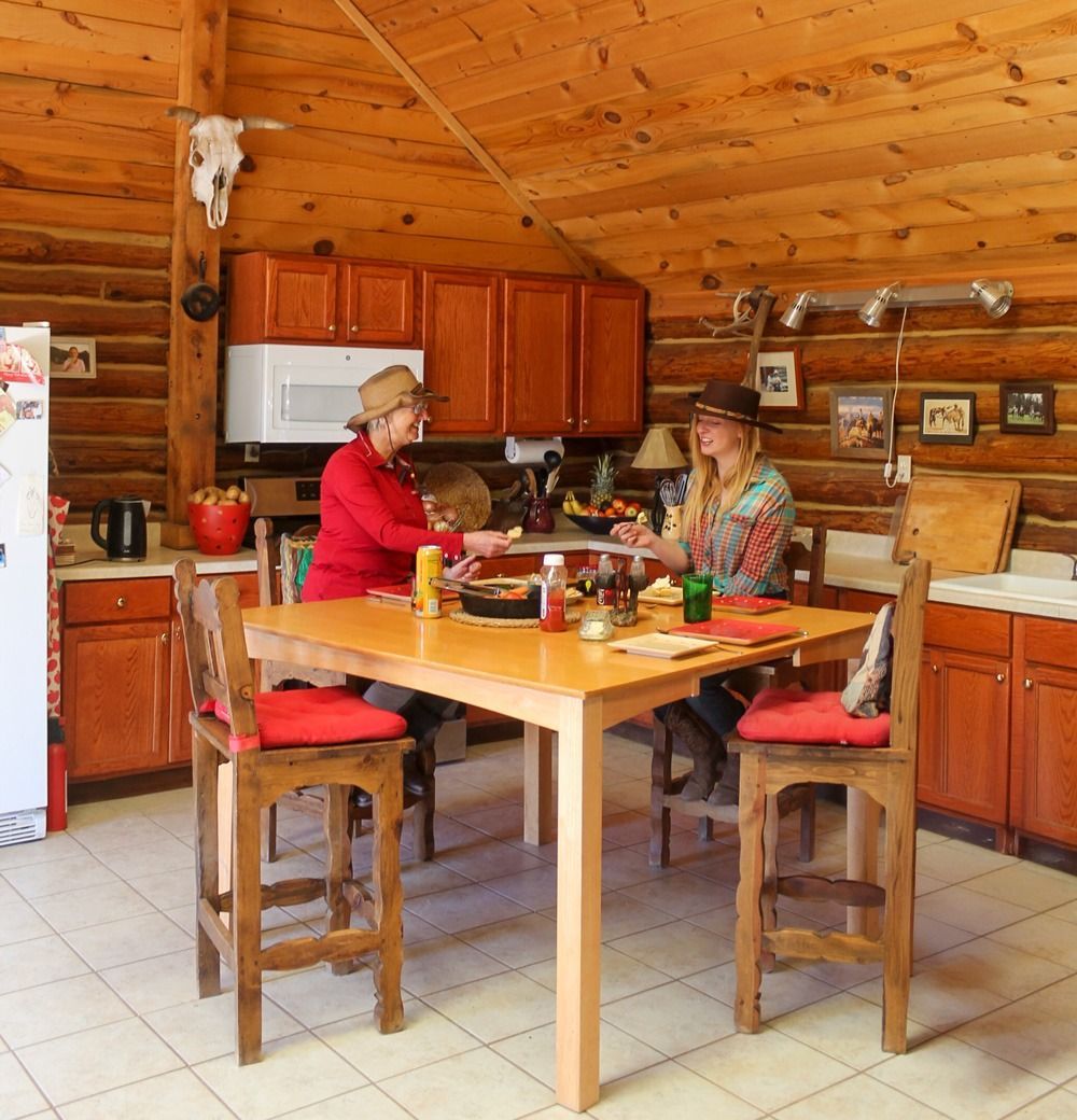 Two people in a log cabin kitchen seated at a wooden table, preparing food.