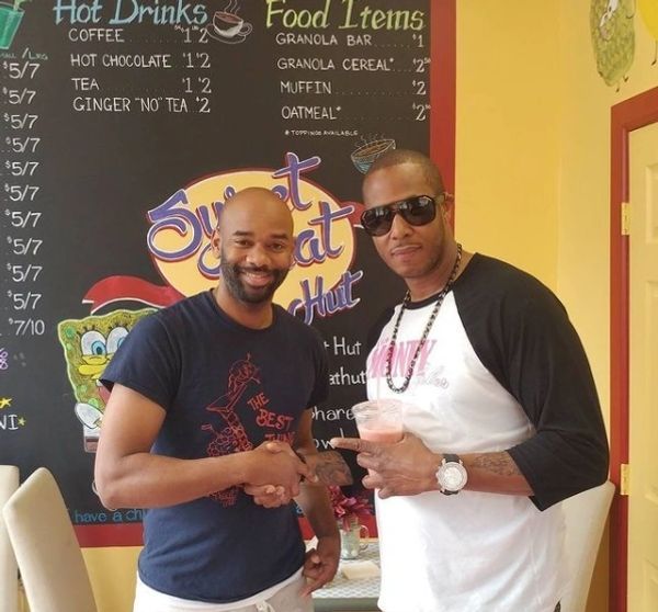 Two men standing in front of a sign that says hot drinks