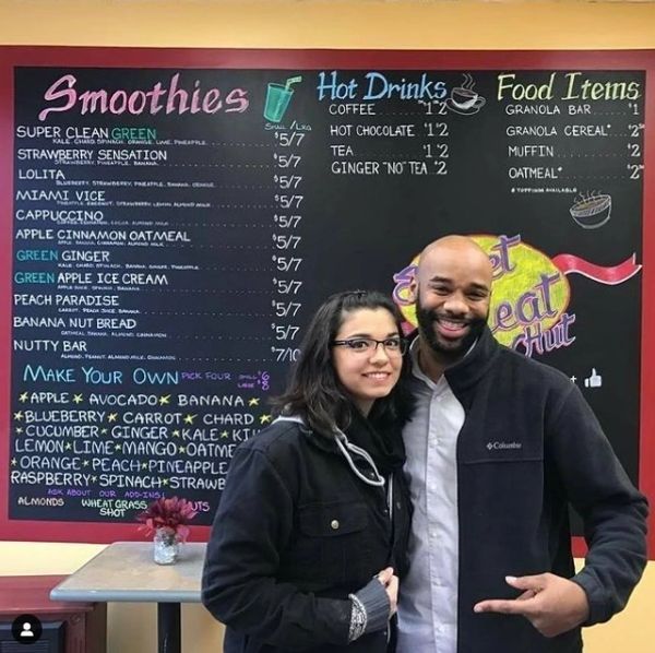 A couple standing in front of a menu that says smoothies hot drinks and food items
