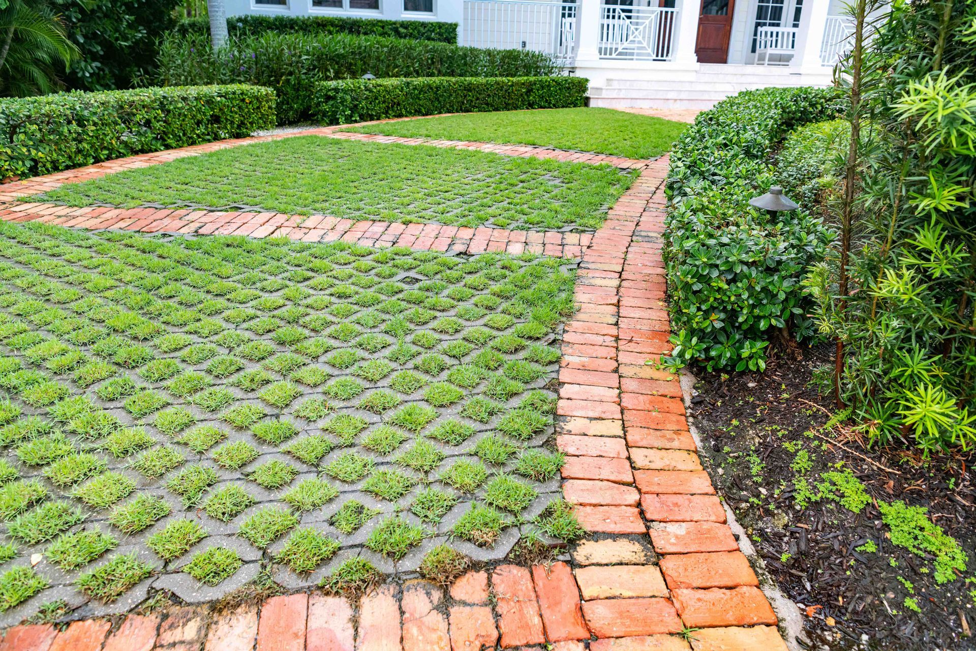 Curved brick driveway with grass pavers and neatly trimmed hedges in a residential yard.