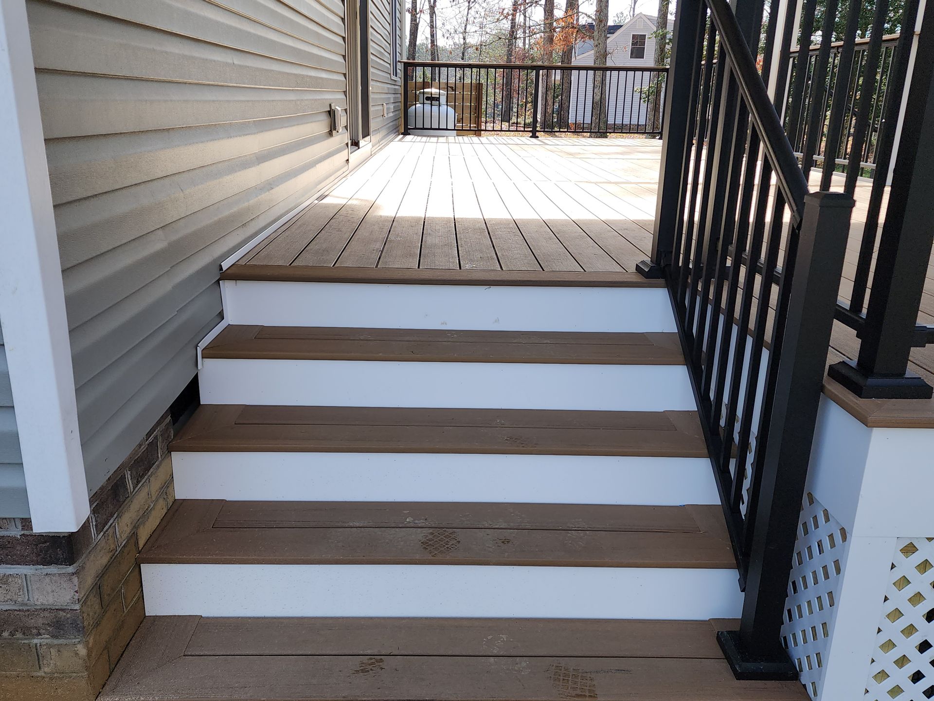 Wooden steps leading up to a deck, with a black railing on the right.