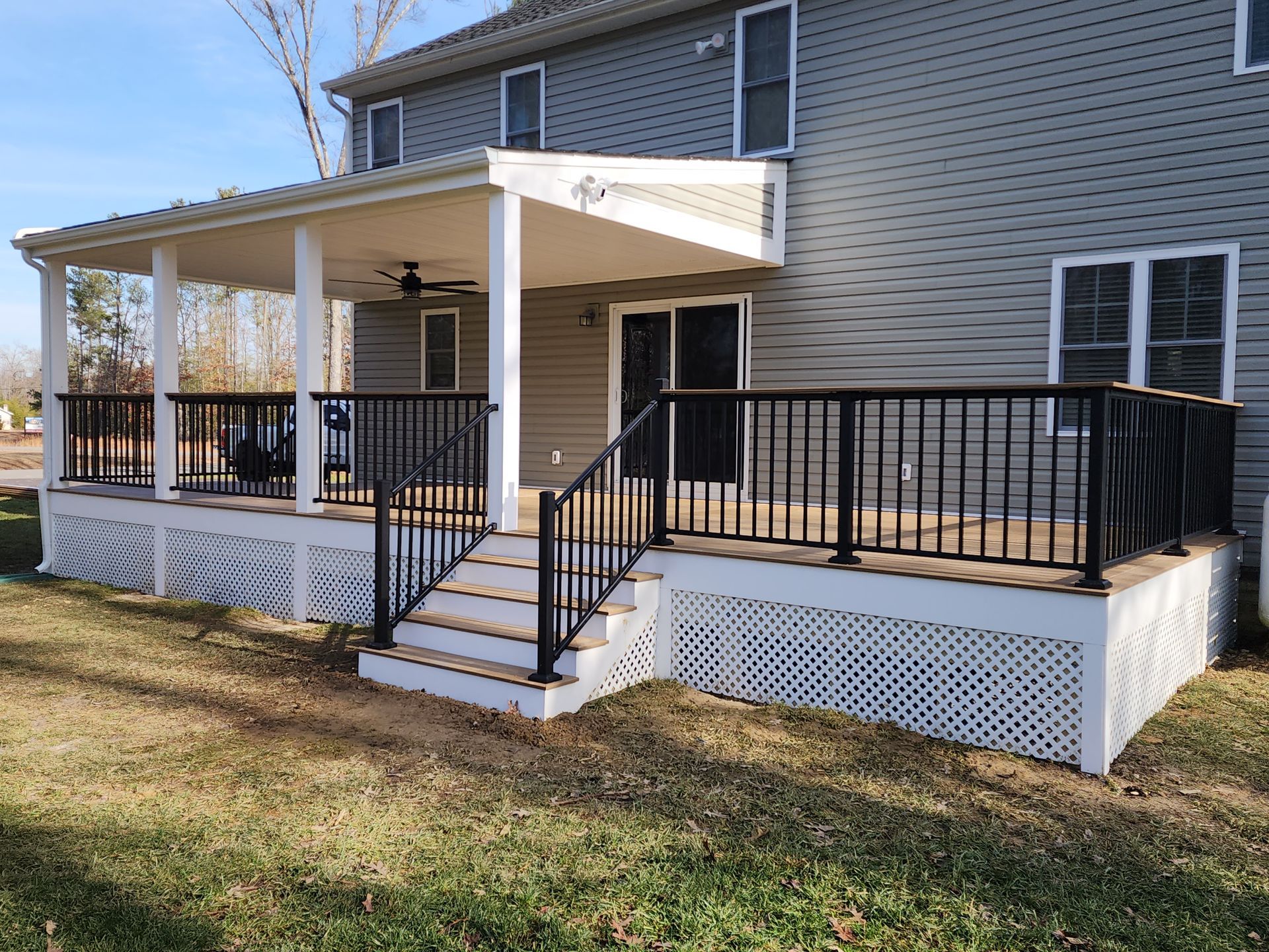 A two-story house with a covered deck and stairs, black railings, and white lattice skirting.