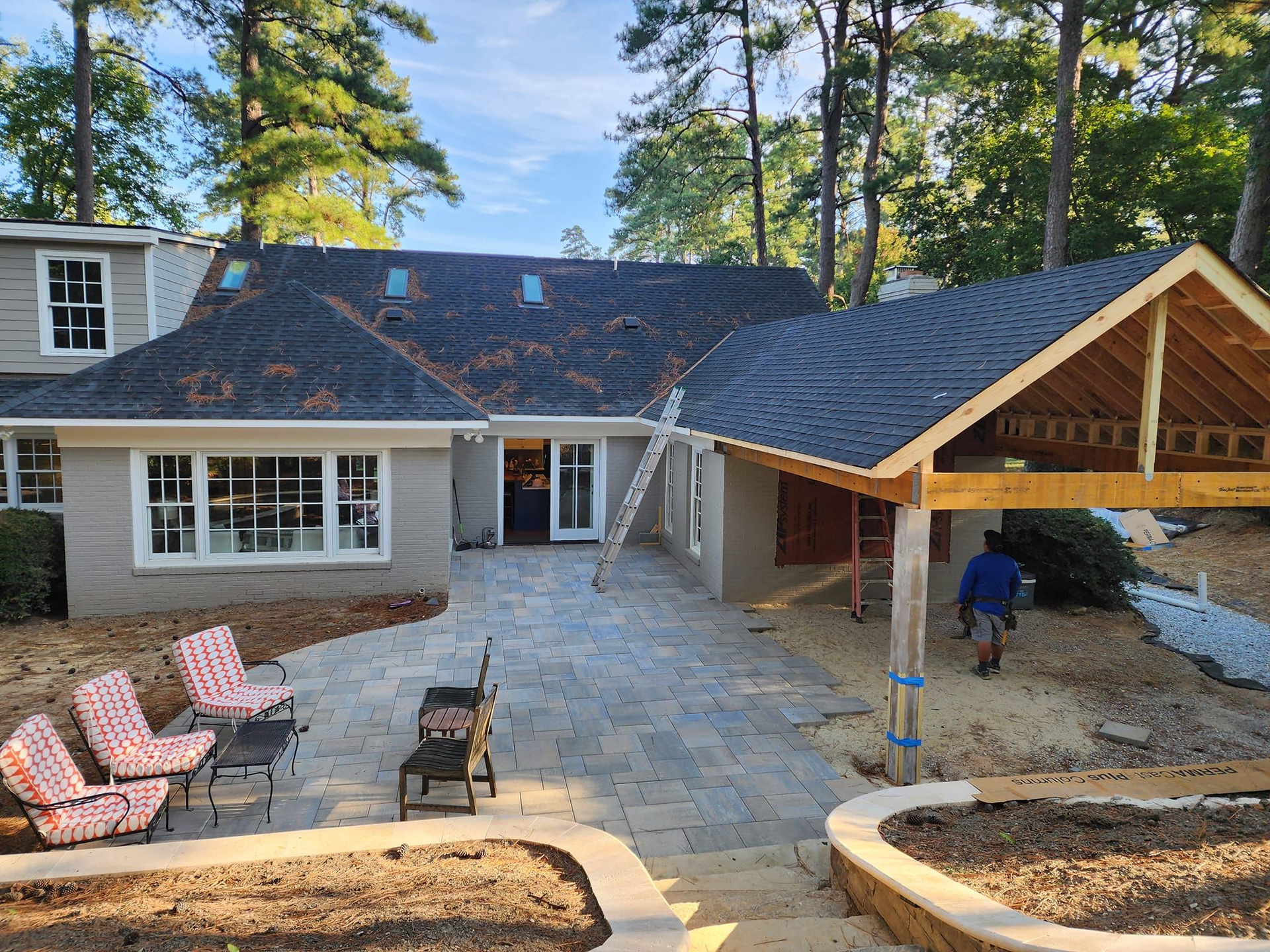 Backyard patio under construction with new roof addition, gravel, and seating. A person walks towards the right.