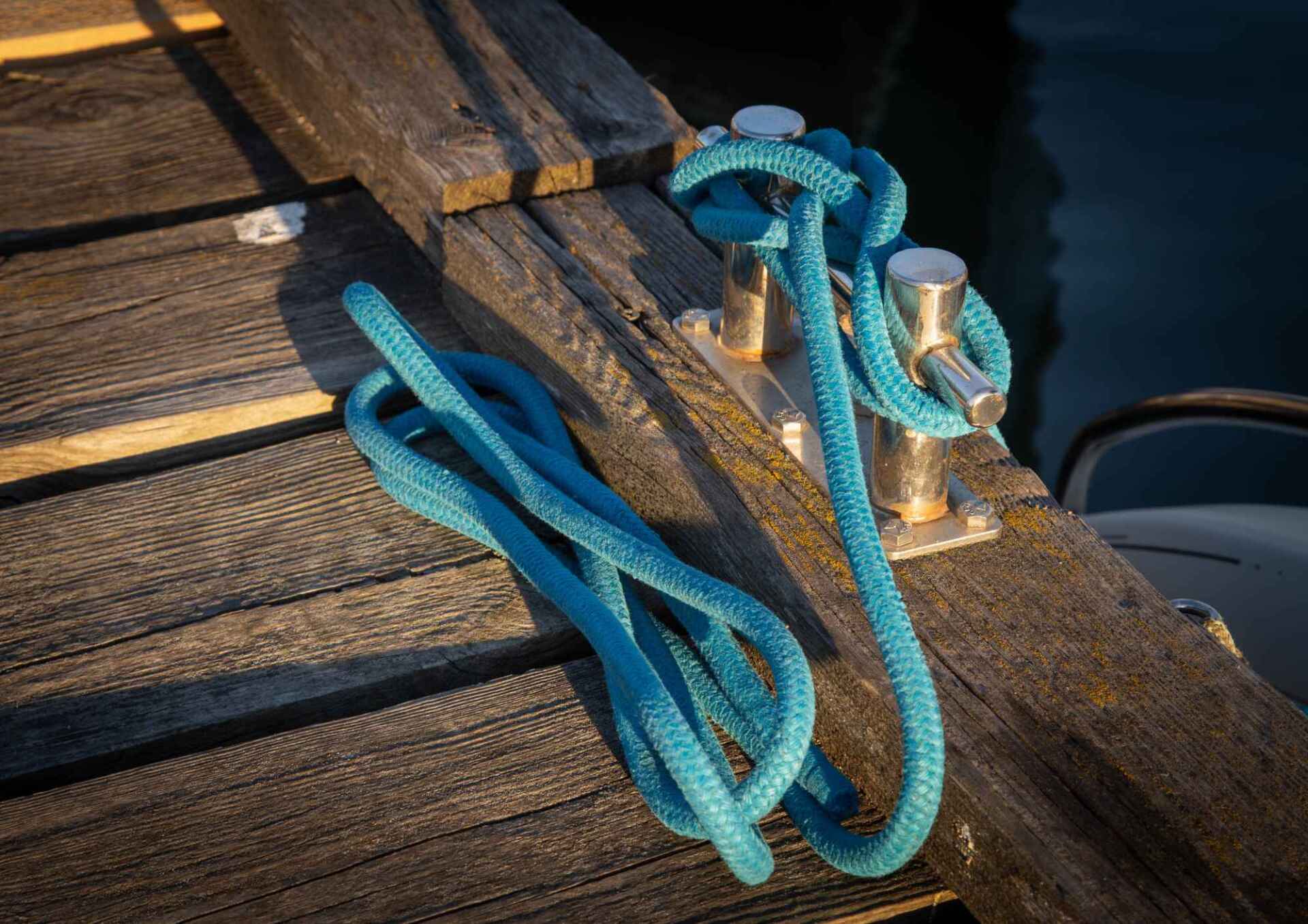 Blue rope tied to a metal cleat on a weathered wooden dock.