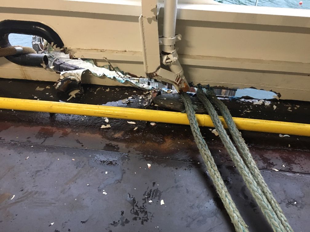 Damaged boat deck: Ropes pass through a torn opening in the side. White, blue, and yellow paint is chipped and scraped.