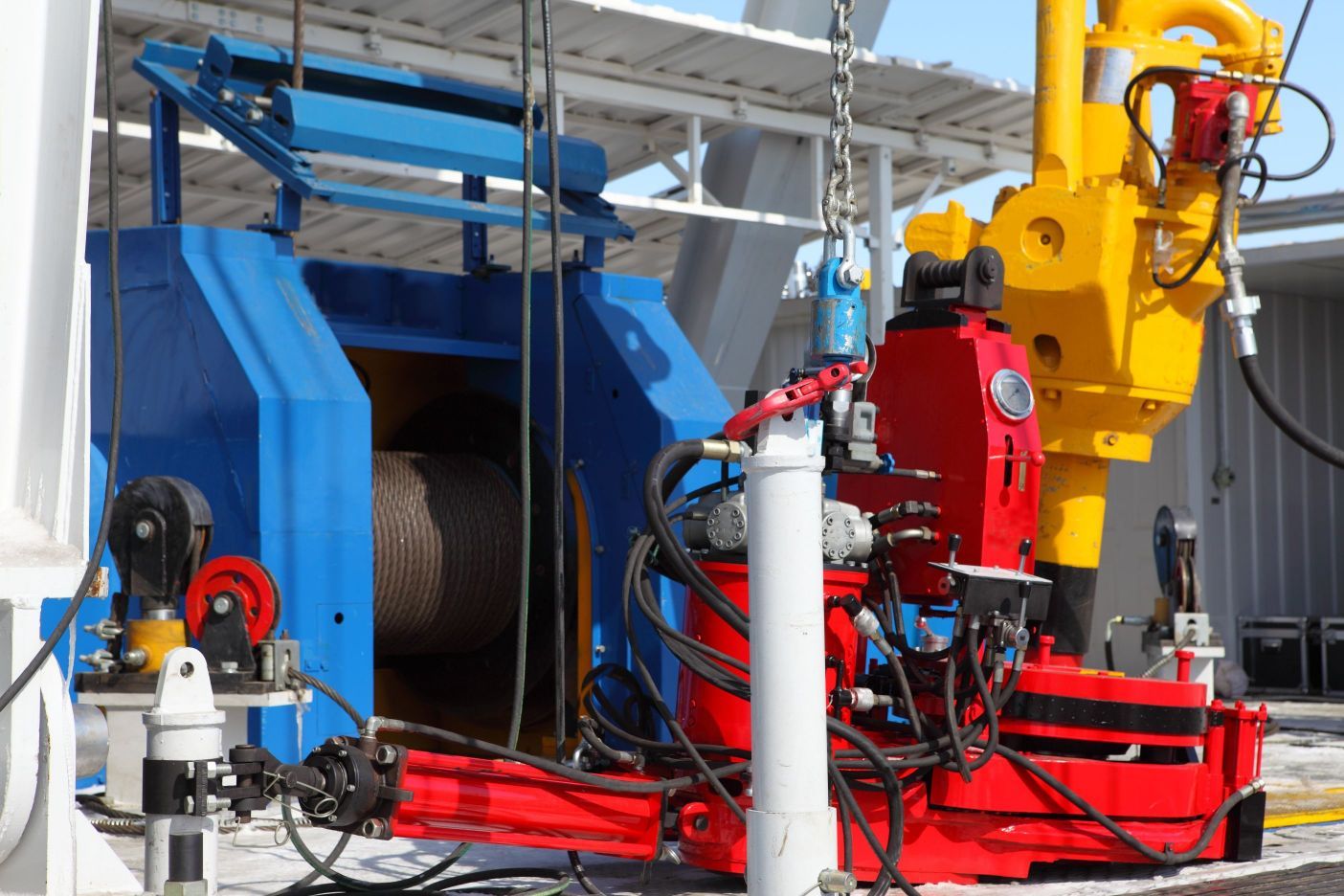 Oil rig machinery, blue and red components, yellow arm. Drilling equipment.