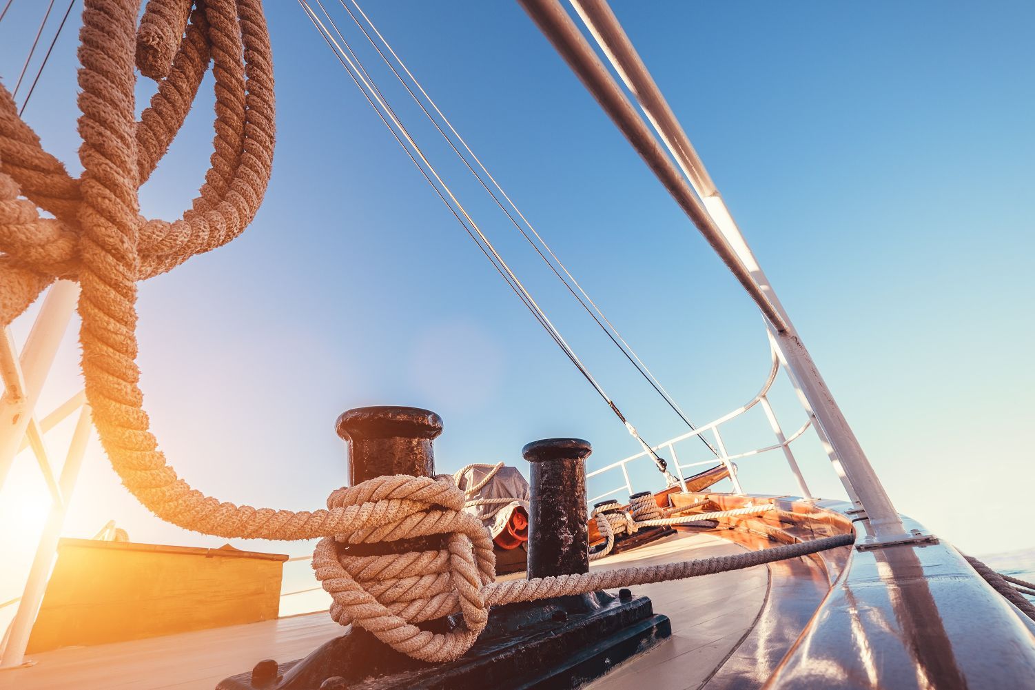Ropes coiled on sailboat deck, rigging, blue sky, and sunshine.