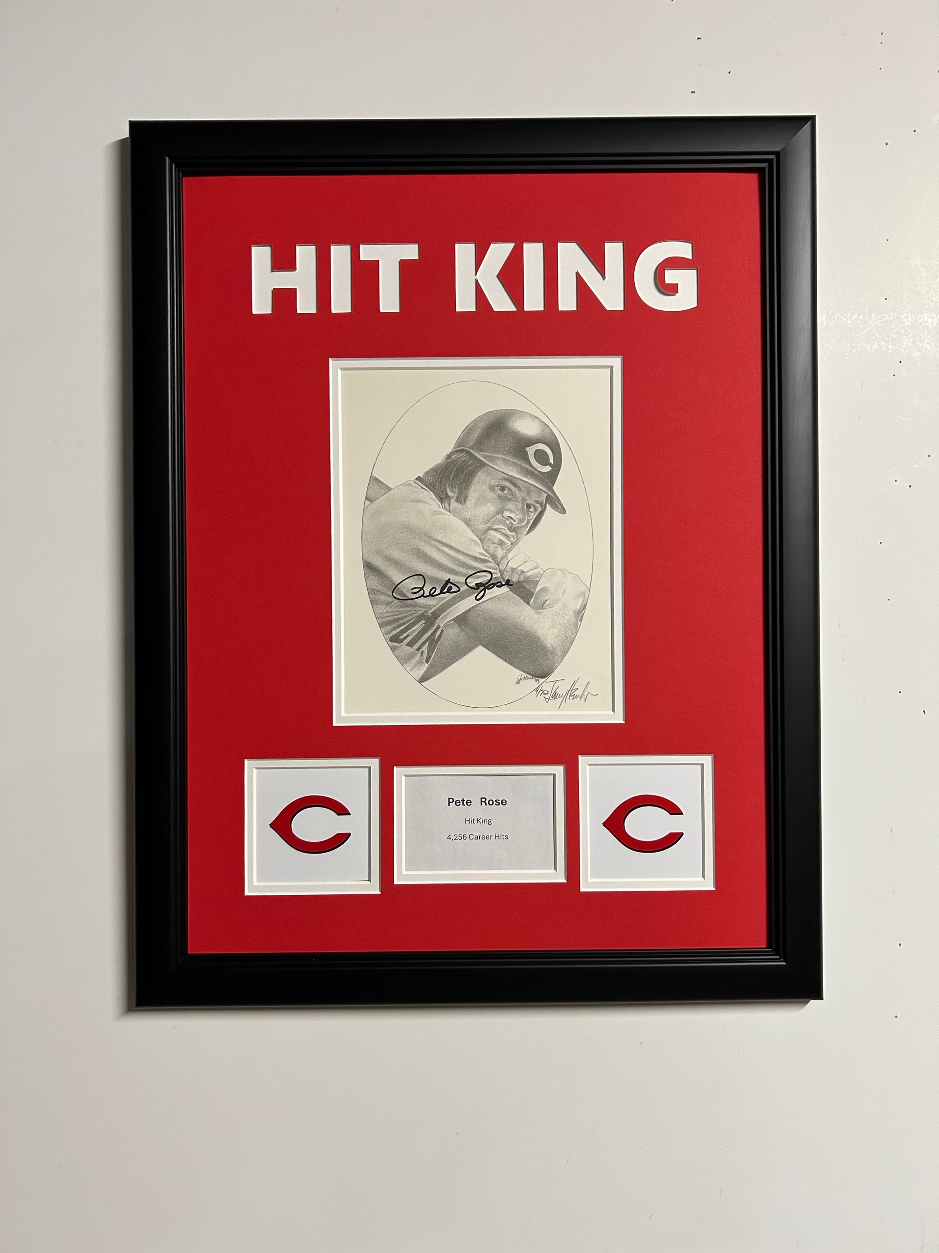 Framed red-and-black “HIT KING” baseball display with a bird sketch and three small cards.