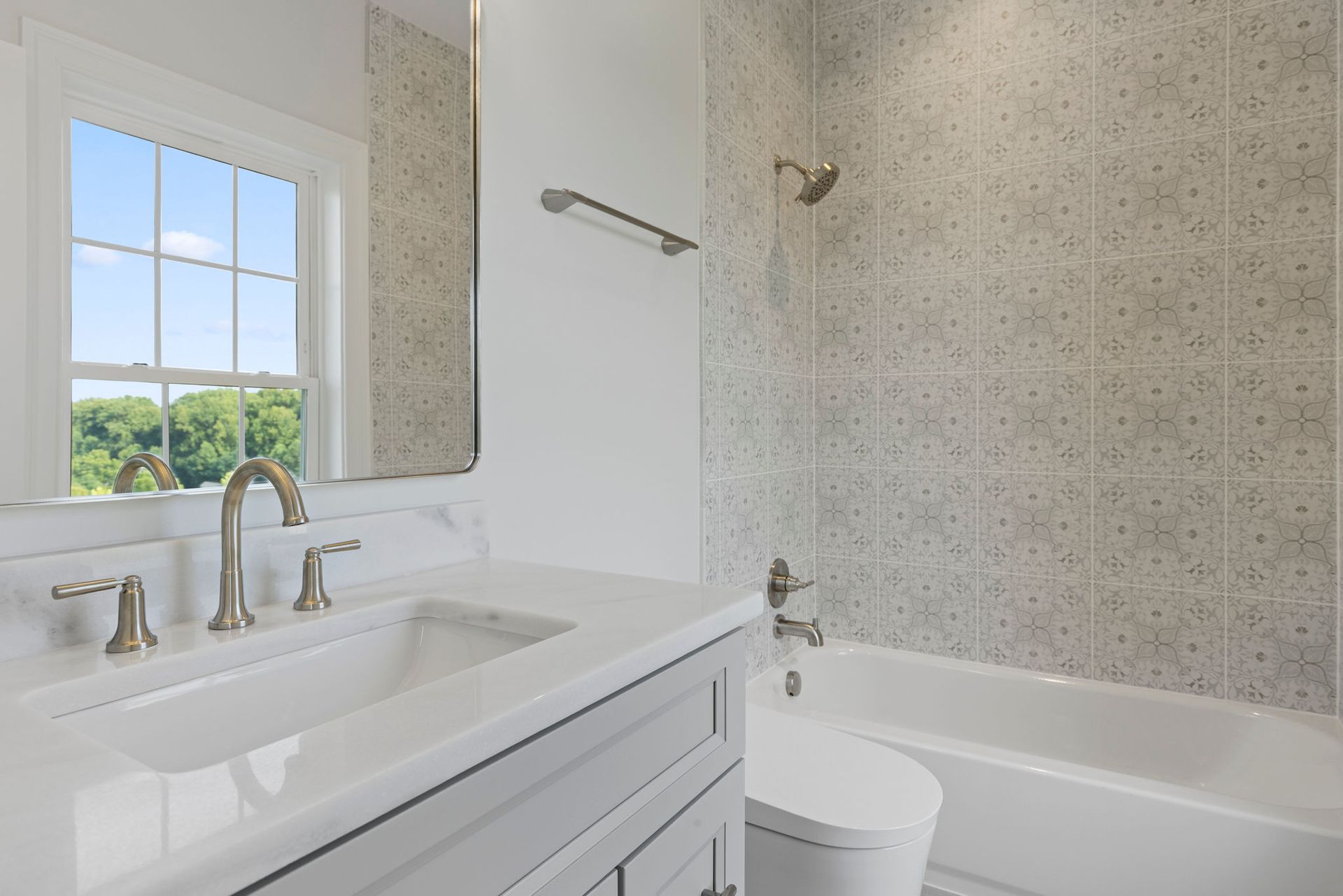 A beautifully renovated guest bathroom with new patterned floor tiles, a sleek floating vanity, and a large, minimalist mirror.