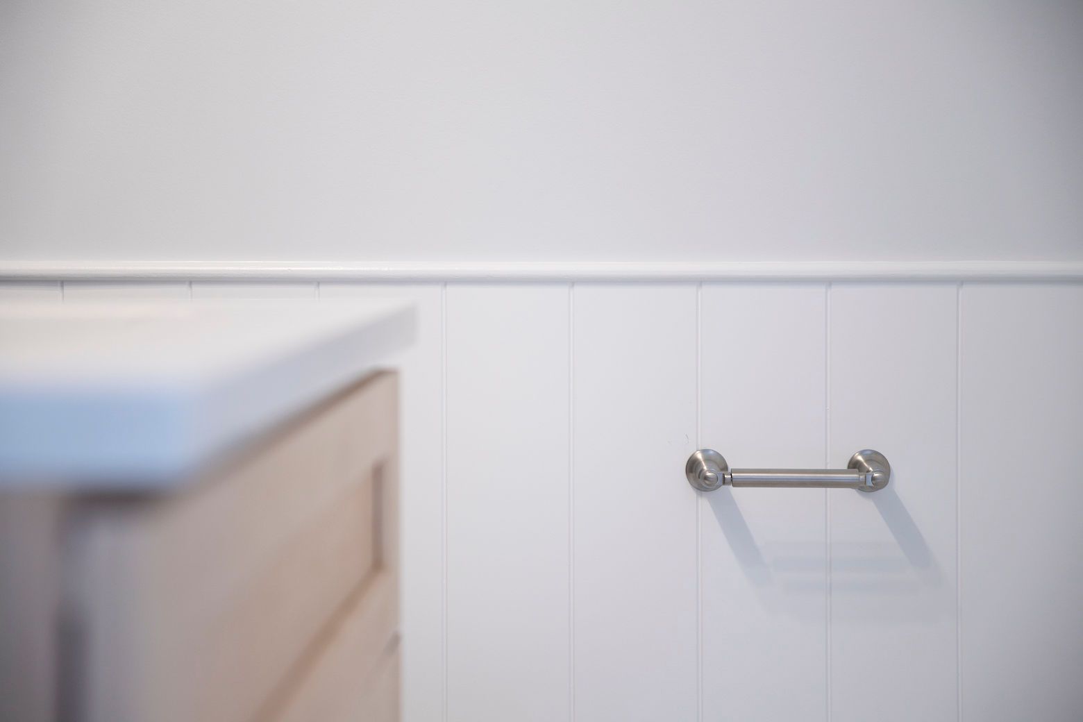 A brushed nickel towel bar on white wainscoting in a new powder room remodel.