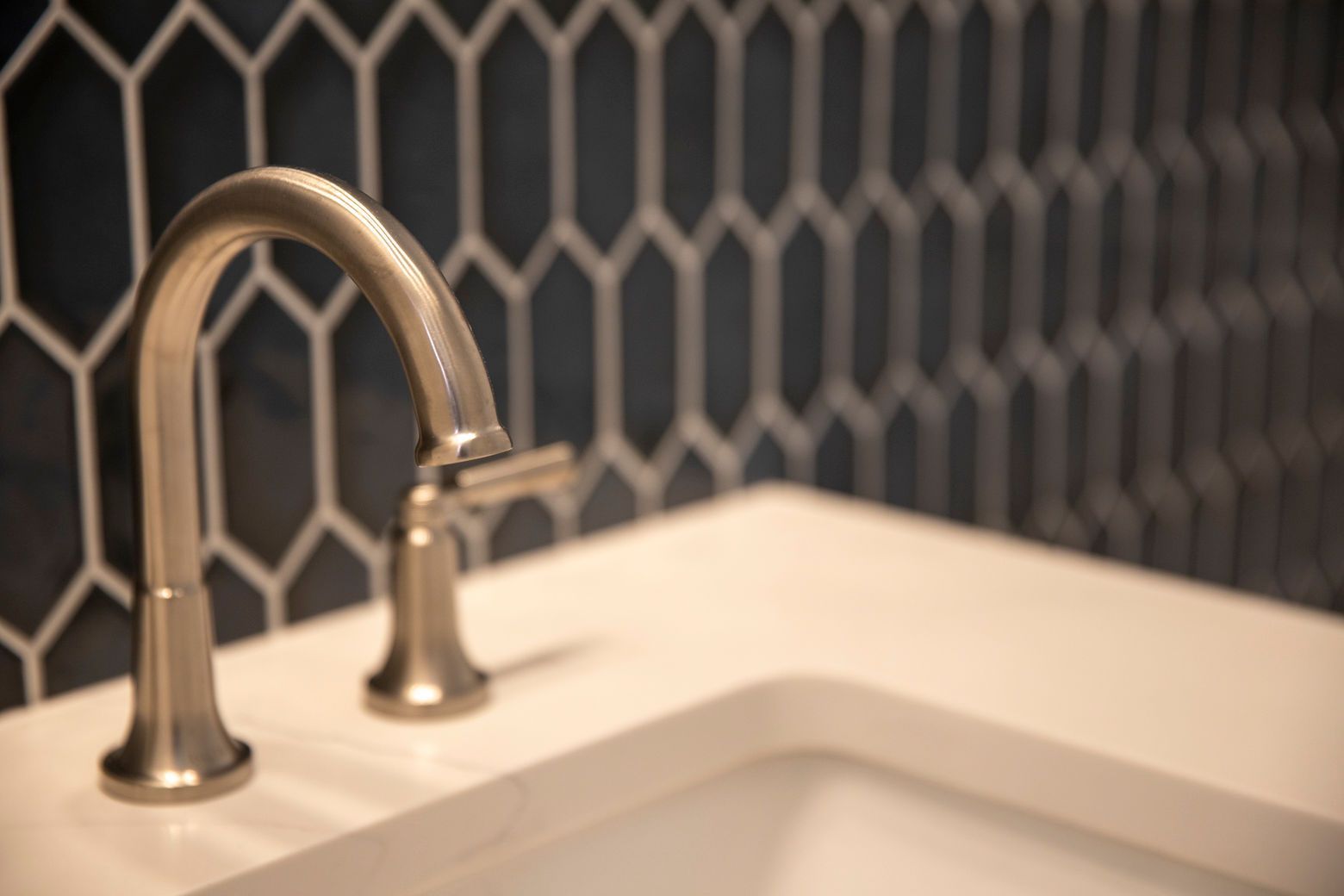A close-up of a brushed nickel faucet on a new vanity with the unique hexagonal tile wall in the background.