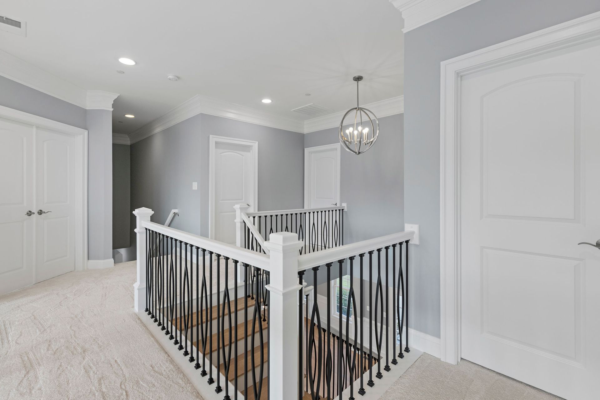Newly renovated staircase featuring modern black metal spindles, a wooden railing, and new gray carpet.