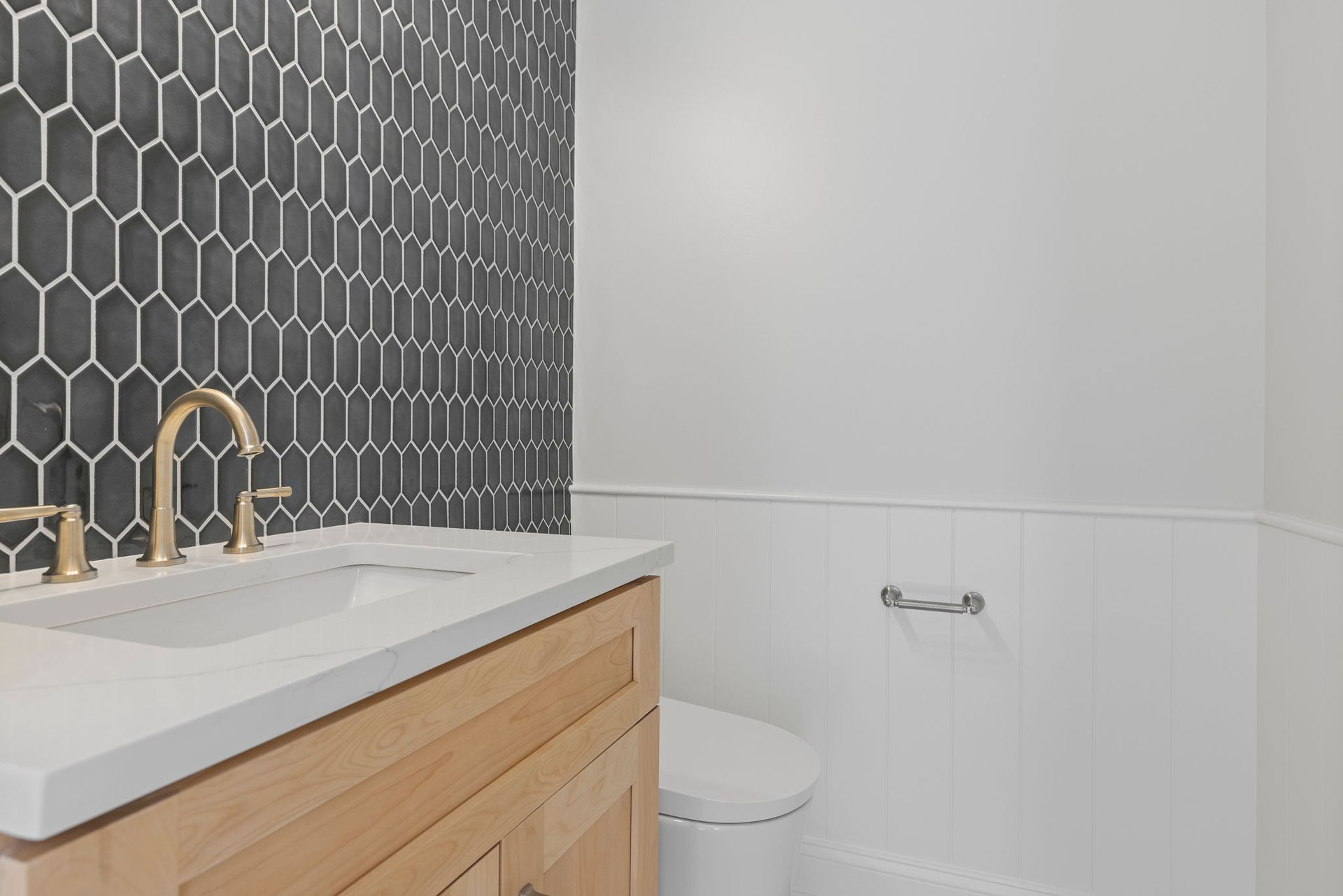  A new natural wood vanity with brushed nickel faucets against a bold, dark hexagonal tile wall in a