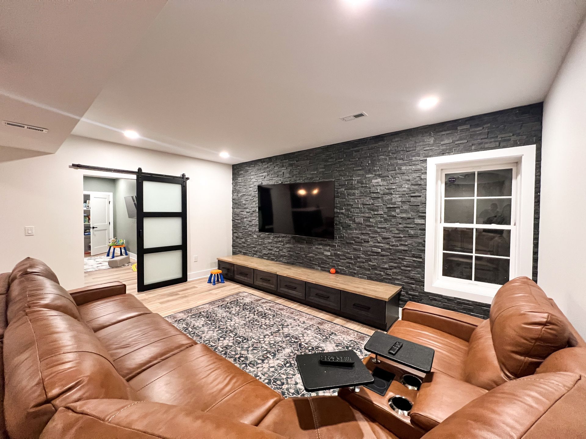 Contemporary finished basement with black focal wall and large television.