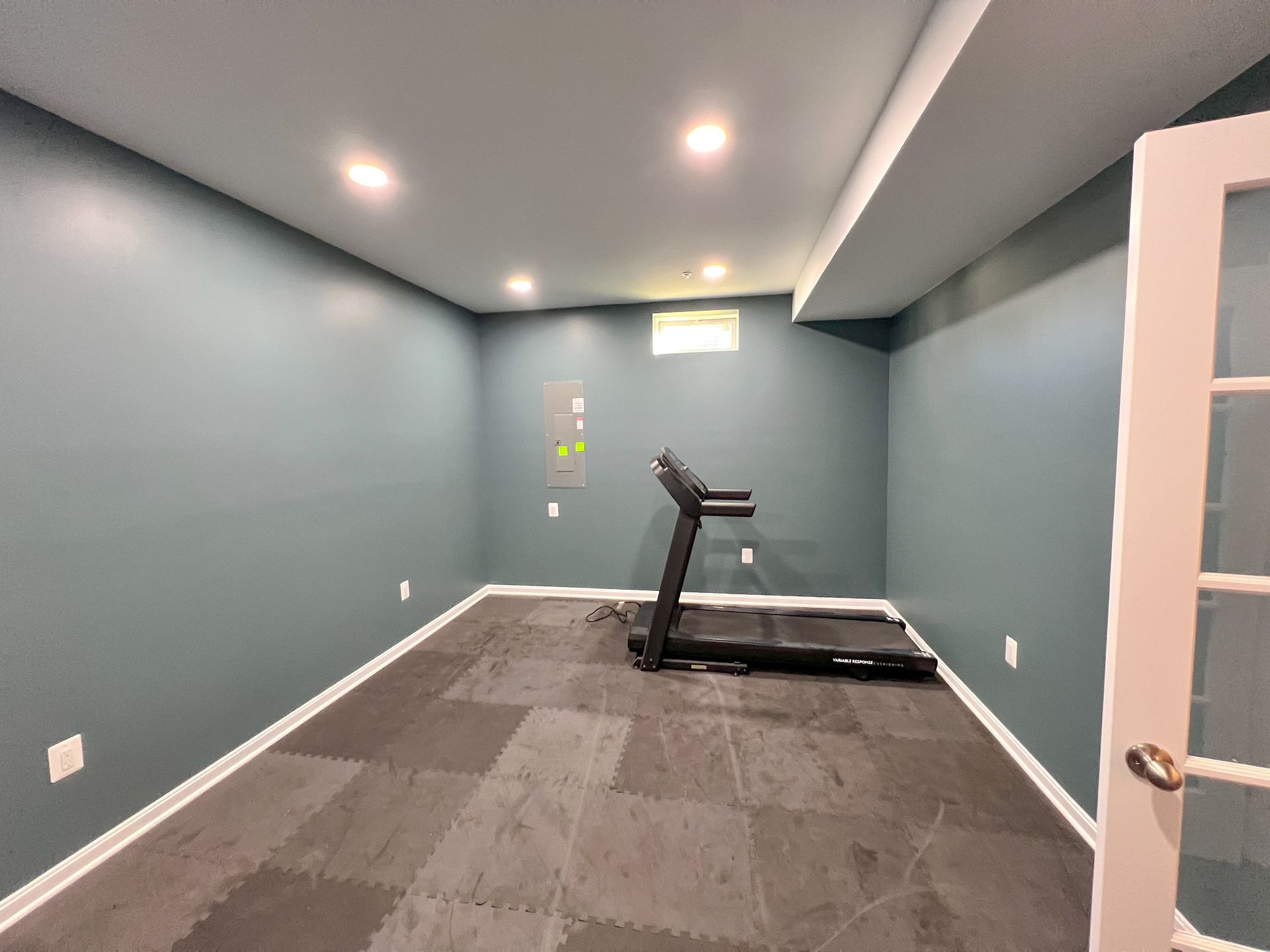 Owings Mills basement gym: Blue-grey walls, recessed lighting, French doors, treadmill, patterned flooring.