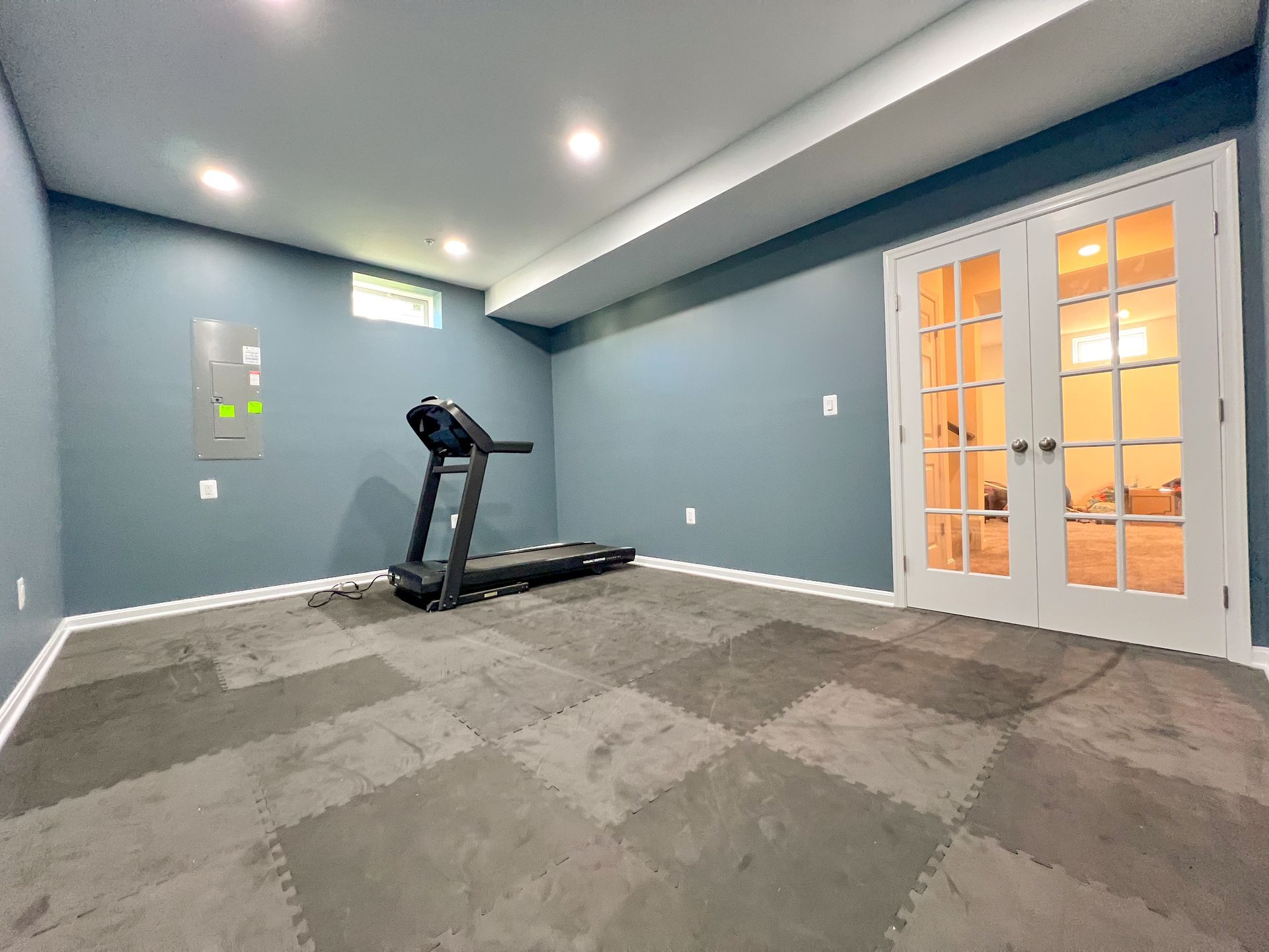 Owings Mills basement gym. Blue-grey walls, drywall ceiling with recessed lights, French doors 