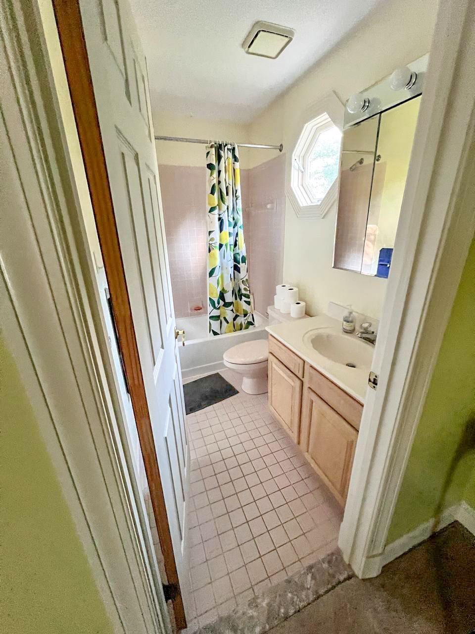  Dated bathroom with light wood vanity and shower curtain.