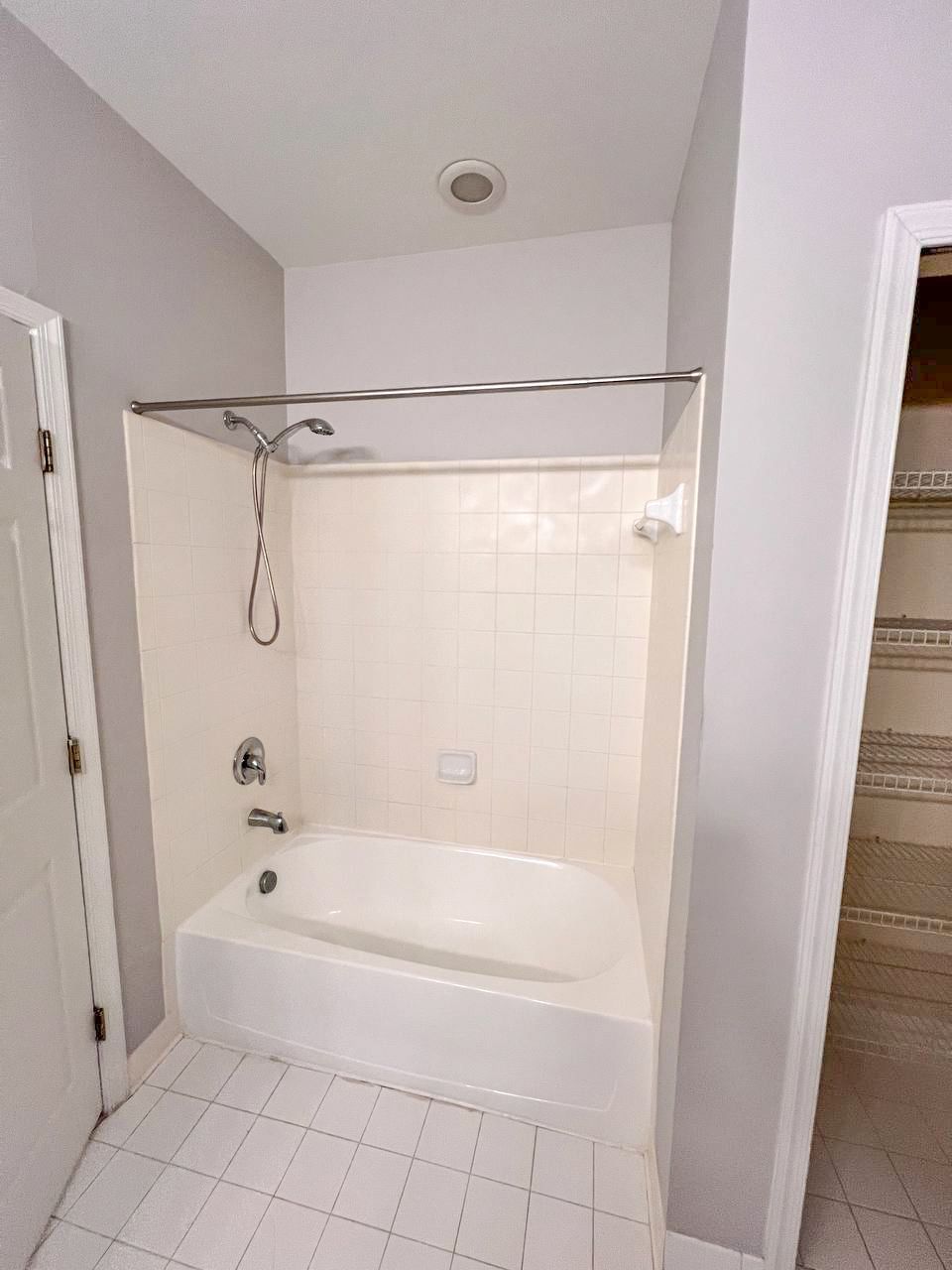 Standard white bathtub/shower combination with white tile surround before renovation.