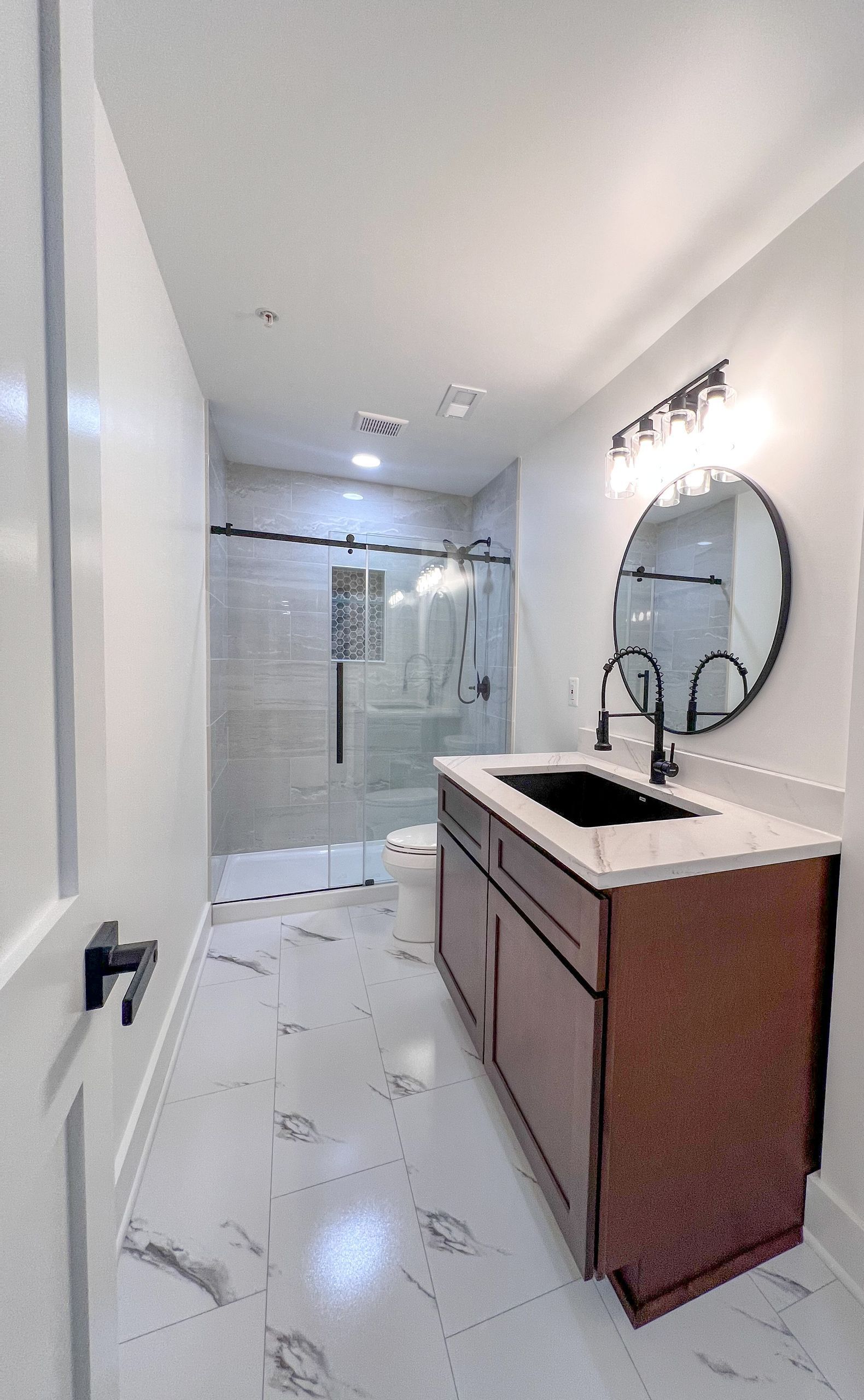 Modern basement bathroom in Reisterstown with a glass-enclosed shower and dark vanity.