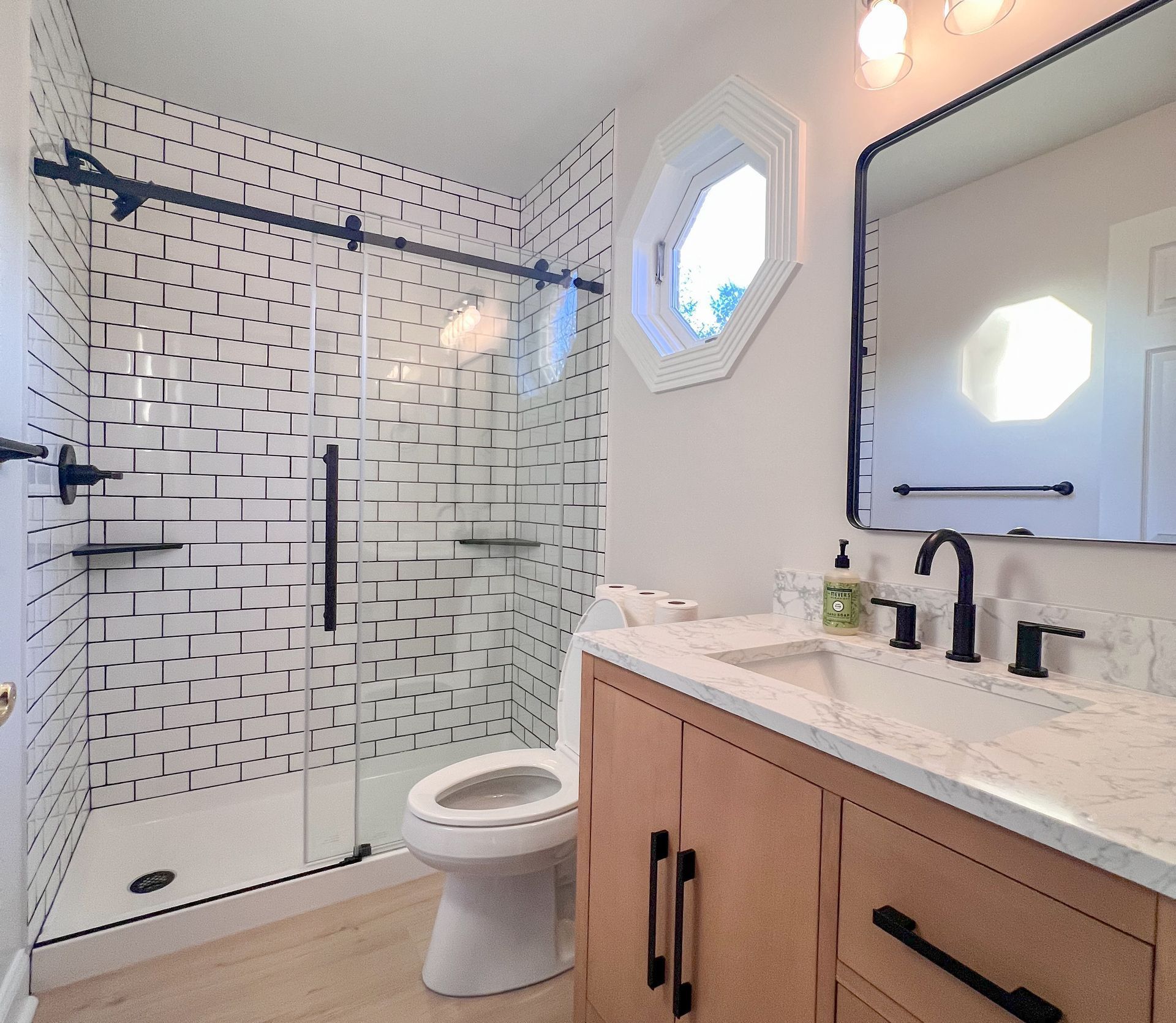 Bright bathroom with walk-in shower, white tile, and light wood vanity.