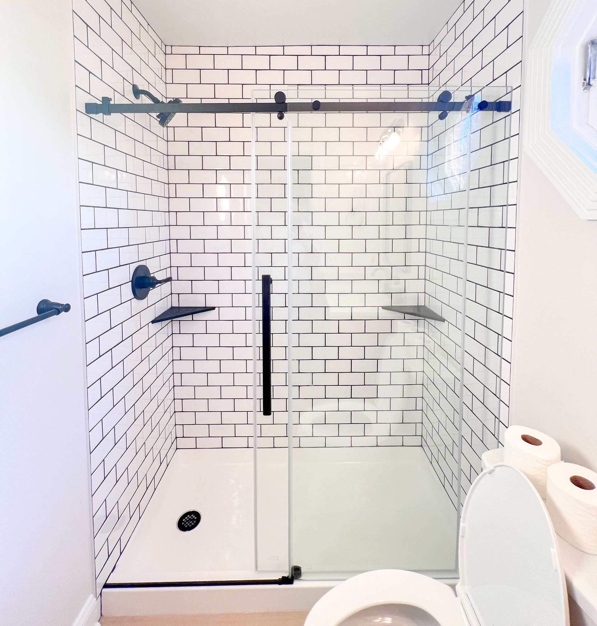 Renovated bathroom with walk-in shower, white tile, and light wood vanity.