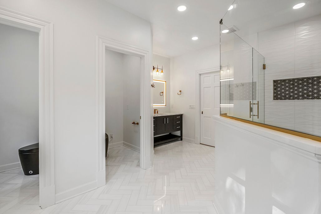 Modern bathroom with new herringbone tile and a view into one of the new, private toilet rooms.