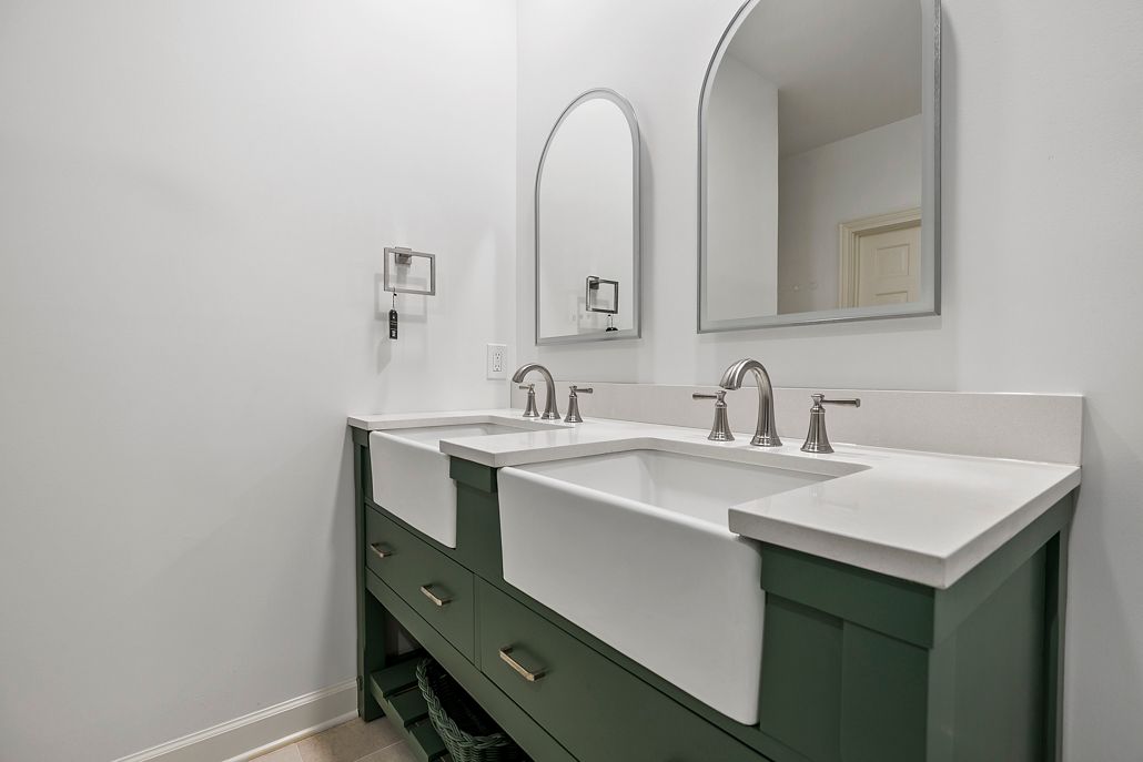 Side-view of a custom-built, dark green vanity with twin farmhouse sinks and modern hardware.