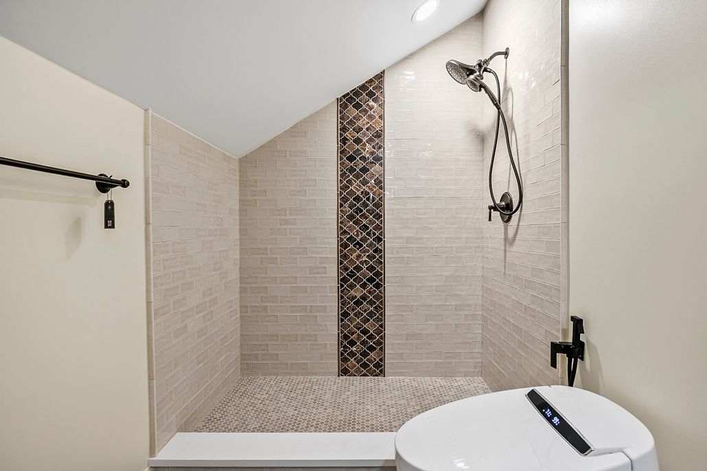 The newly installed walk-in shower with a light subway tile and a striking vertical mosaic accent wall.